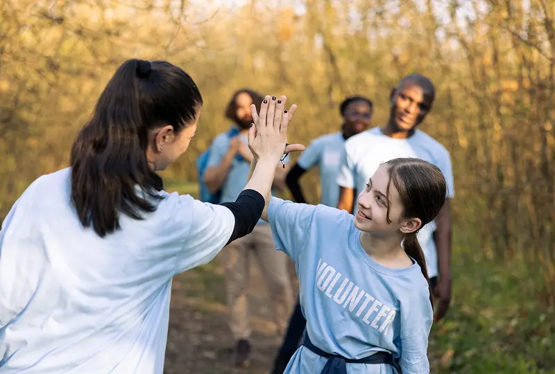 Volunteers high-fiving outdoors in matching shirts.