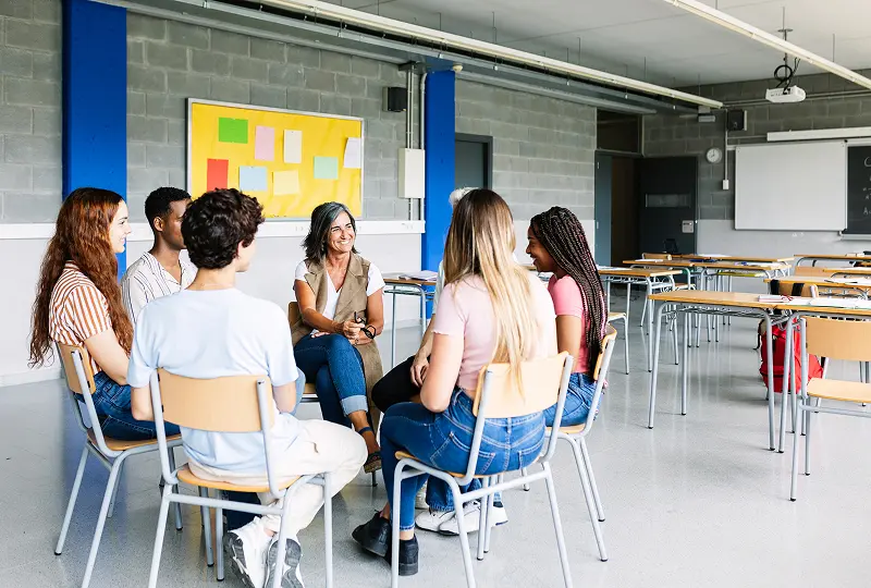 Classroom discussion with teacher and students seated.