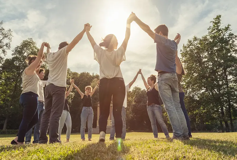 People holding hands in a circle outdoors.