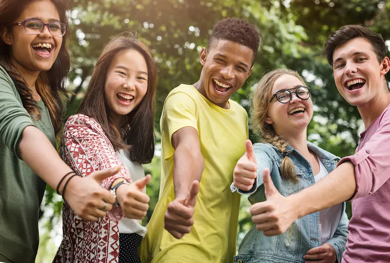 Group of friends giving thumbs up outdoors.